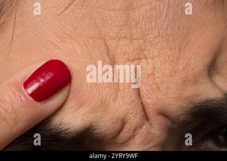 Nahaufnahme der Hand einer Frau mit rotem nagellack, die Falten auf der Stirn berührt und die Probleme der alternden Haut hervorhebt Stockfoto