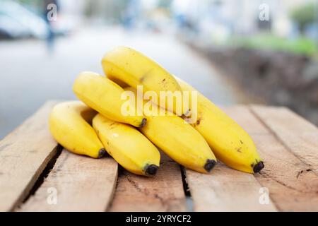 Ein gelber Zweig reifer Bananen liegt auf einer Holzbank. Stockfoto