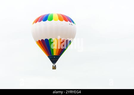 Der Heißluftballon Rainbow schwingt vor einem klaren, weißen Himmel und bietet ein lebendiges Spektakel Stockfoto