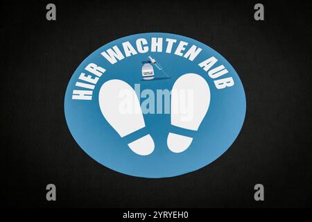 Bodenschild mit sozialer Distanz auf Niederländisch, das die Leute anweist, zu warten und Händedesinfektionsmittel zu verwenden, wobei Hygiene- und Sicherheitsmaßnahmen hervorgehoben werden. Stockfoto