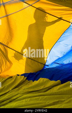 Silhouette einer Frau mit Blumen hinter ukrainischem Flaggenzelt, die Hoffnung und Widerstandsfähigkeit repräsentiert Stockfoto