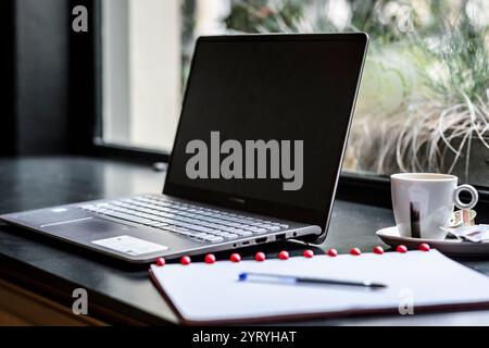 Laptop, Notebook und Espresso an einem modernen Arbeitsplatz am Fenster, ideal für Fernarbeit, Studium oder kreative Projekte. Stockfoto