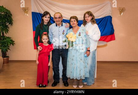 Eine russische Familie feiert einen goldenen Hochzeitstag (50 Jahre). Die Großeltern sind elegant gekleidet und von ihren Enkeln Smili umgeben Stockfoto