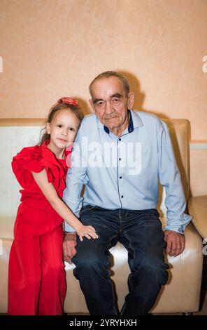 Ein russischer Großvater und seine achtjährige Enkelin feiern ihren Geburtstag. Der Großvater, 76 Jahre alt, und das Mädchen sind festlich gekleidet, Shar Stockfoto