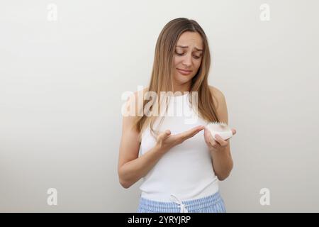 Frustrierte junge Frau mit Haarausfall-Problem hält Haarbürste und zeigt sich nach dem Kämmen auf einem Haufen gefallener Haare. Alopezie, endokrine Störungen, hormonelle Störungen Stockfoto