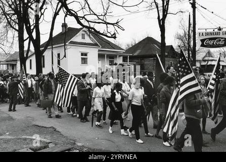 Teilnehmer, einige mit amerikanischen Flaggen, marschierten 1965 auf dem bürgerrechtsmarsch von Selma nach Montgomery, Alabama. Die Selma-Montgomery-Märsche waren drei Protestmärsche, die 1965 auf der 54 km langen Autobahn von Selma, Alabama, in die Hauptstadt Montgomery abgehalten wurden. Die Märsche wurden von gewaltlosen Aktivisten organisiert, um den Wunsch afroamerikanischer Bürger zu demonstrieren, ihr verfassungsmäßiges Wahlrecht unter Missachtung der segregationistischen Unterdrückung auszuüben. Durch die Hervorhebung der rassischen Ungerechtigkeit trugen sie zur Verabschiedung des Voting Rights Act im Jahr 1965 bei. Stockfoto