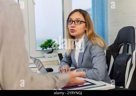 Die Geschäftsfrau betrachtet ihre Kollegen mit Unmut über die Arbeit. Eine weibliche Mitarbeiterin im Büro kommuniziert mit ihren Mitarbeitern. Die böse Frau ist es Stockfoto