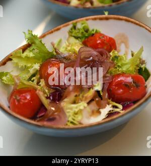 Salat mit Kirschtomaten, Zwiebeln und Salat in einer blauen Schüssel Stockfoto