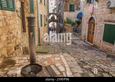 Eingang von Kotors Altstadt, der zu den ummauerten Befestigungsanlagen der Stadt führt; Details umfassen die unverwechselbaren Kopfsteinpflasterstraßen und Steinhäuser. Stockfoto