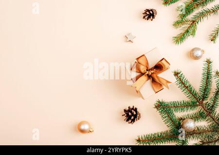 Elegante Geschenkbox mit goldenem Band, Tannenzweigen, Tannenzapfen und festlicher Dekoration auf beigefarbenem Hintergrund für weihnachtliche Atmosphäre. Draufsicht, Stockfoto