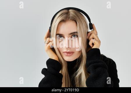 Eine schöne junge Frau mit langen blonden Haaren posiert mit Kopfhörern, eingetaucht in Musik. Stockfoto