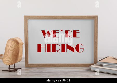 Tafel mit Text We're Hiring, Notizbücher und dekorativer Vogel auf Holztisch. Personalabteilung Stockfoto