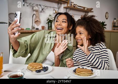 Mutter und Tochter teilen ein Lächeln, während sie ein Selfie beim Frühstück mit Pfannkuchen machen. Stockfoto