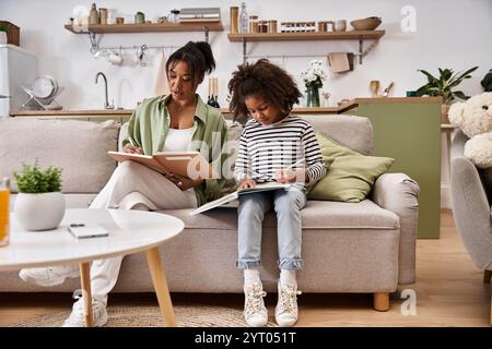 Mutter und Tochter sitzen nebeneinander auf einem Sofa und arbeiten gerne an ihren Kunstprojekten. Stockfoto