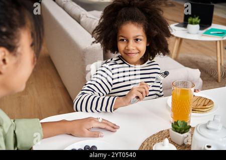 Mutter und Tochter teilen sich ein gemütliches Frühstück mit Pfannkuchen und Saft am Küchentisch. Stockfoto