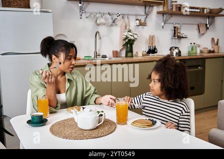 Mutter und Tochter teilen sich ein fröhliches Frühstück und genießen zusammen Pfannkuchen und Getränke. Stockfoto