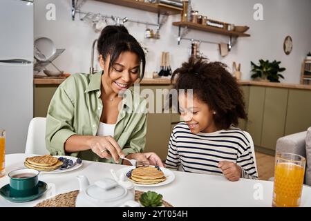 Eine Mutter und ihre Tochter genießen zu Hause ein fröhliches Frühstück mit Pfannkuchen und Beeren. Stockfoto