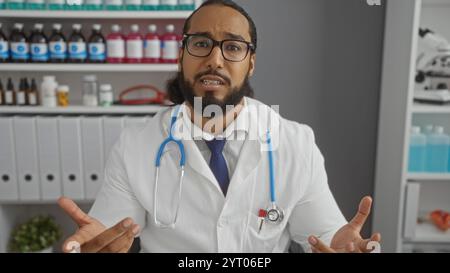Mann im Krankenhaus mit weißem Mantel und Stethoskop in einem klinischen Umfeld dargestellt als erwachsener arabischer Arzt mit einem Bart verwickelt Stockfoto