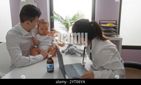 Der Vater hält den Jungen, während die Kinderärztin das Kind im Krankenhauszimmer untersucht, wobei die Pflege und familiäre Atmosphäre zum Ausdruck kommt. Stockfoto