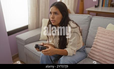 Junge Frau, die Videospiele in einem Wohnzimmer spielt und eine entspannte Atmosphäre mit lässiger Kleidung und fokussiertem Ausdruck bietet. Stockfoto