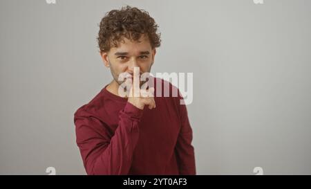 Junger hispanischer Mann mit lockigem Haar, der roten Pullover trägt, der eine ruhige Geste über weißem Hintergrund macht Stockfoto