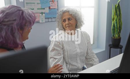 Reife Frauen diskutieren Strategie in einem Büro, wobei eine ältere Frau und eine Frau mittleren Alters sich mit Dokumen an einem Arbeitstreffen im Innenbereich beteiligen Stockfoto