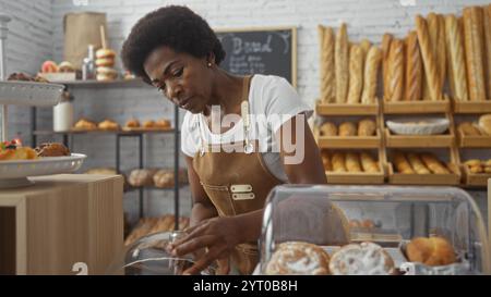 Frau, die in der Bäckerei arbeitet und Backwaren mit Regalen mit Brot und Backwaren im Hintergrund arrangiert Stockfoto