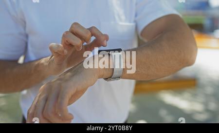 Hispanischer Mann, der Smartwatch im urbanen Park verwendet, um praktische Technik in einer Outdoor-Stadtumgebung zu veranschaulichen. Stockfoto