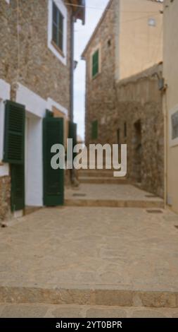 Verschwommene Outdoor-Szene auf mallorca, spanien, mit einem unscharfen Blick auf rustikale Steinhäuser mit grünen Fensterläden und Steintreppen in einer engen Gasse Stockfoto