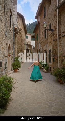 Frau, die in valldemossa, einem charmanten Dorf auf der Insel mallorca, in einer engen, kopfsteingepflasterten Straße, umgeben von rustikalen Steinhäusern, spaziert Stockfoto