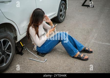 Eine Frau in Jeans hat Probleme mit dem Auto, während sie ihr Telefon dringend benutzt Stockfoto