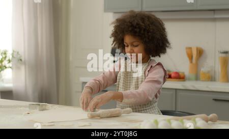 Kleines afroamerikanisches Mädchen tragen Schürze Kind Kind ethnische Tochter Entwicklung lernen zu kochen Backen Kochen alleine in der Küche zu Hause Mehl zubereiten Stockfoto