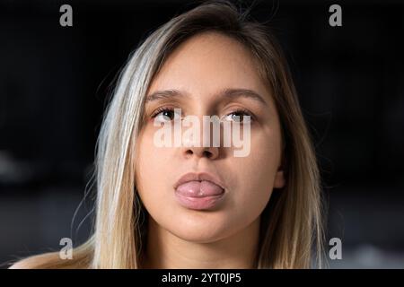 Attraktive positive Frau, blond, grimmig, lächelt, zieht Aufmerksamkeit auf sich, der Blick im Spiegel zeigt die Zunge spielerisch Stockfoto