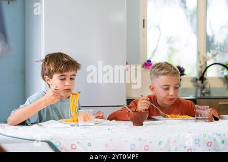 Zwei junge Brüder genießen ein Essen mit Spaghetti mit Tomatensauce, sitzen an einem Tisch in ihrer Küche Stockfoto