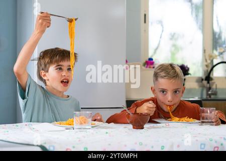 Zwei Brüder essen Spaghetti mit Tomatensauce und haben Spaß zu Hause Stockfoto