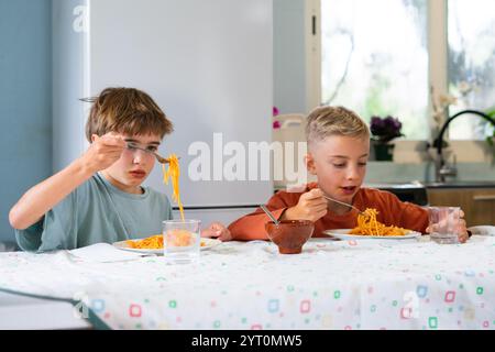 Zwei junge Brüder genießen eine Mahlzeit mit Spaghetti mit Tomatensauce, sitzen an einem Tisch in ihrer Küche Stockfoto