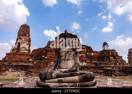 Eine Buddha-Statue sitzt auf einer Steinplattform vor einem großen Gebäude. Die Statue ist von einer grasbewachsenen Fläche umgeben Stockfoto