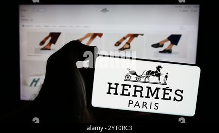 In dieser Abbildung hält eine Person ein Handy mit dem Logo des französischen Luxusunternehmens Hermes International S.A. vor der Webseite. Stockfoto