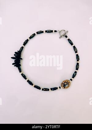 Schwarze Halskette mit Steinperlen auf rosafarbenem Hintergrund aus nächster Nähe von oben. Hämatit, Magnetit Halbedelstein Choker, unregelmäßige Form, Damenschmuck Stockfoto