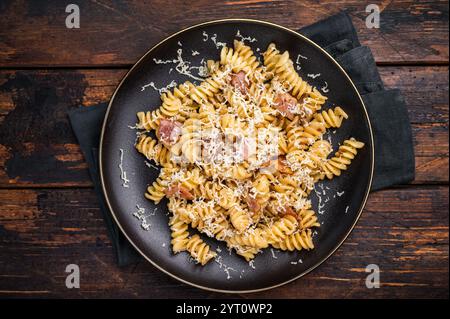 Italienische Carbonara-Pasta mit knusprigen Speckstückchen auf einem Teller. Hölzerner Hintergrund. Draufsicht. Stockfoto
