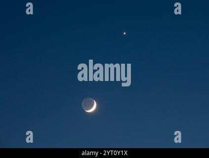 Der Planet Venus in unmittelbarer Nähe eines Halbmondes kurz nach Sonnenuntergang am 4. Dezember 2024. Stockfoto