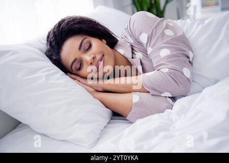 Die junge Frau schläft friedlich in einem bequemen Pyjama mit Punktmuster und erholt sich in einem gemütlichen, hellen Schlafzimmer Stockfoto