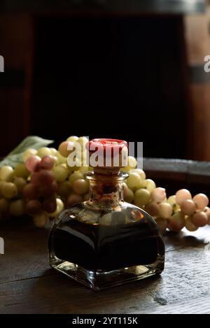 Traditioneller Balsamico-Essig aus Modena in einer kleinen Flasche auf einem Holzfass Stockfoto