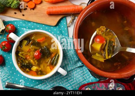 Heiße Gemüsesuppe in einer Steingut-Pfanne mit einer Kelle dampfender Suppe mit Zutaten Stockfoto