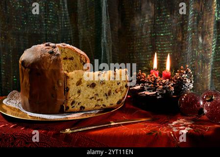 Weihnachts-Panettone mit Scheiben auf einem goldenen Teller, mit beleuchteten Kerzen und Dekorationen in der Nähe. Typisch italienisches Dessert Stockfoto