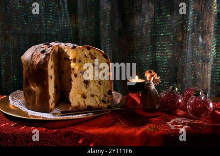 Weihnachts-Panettone mit Scheiben auf einem goldenen Teller, mit beleuchteten Kerzen und Dekorationen in der Nähe. Typisch italienisches Dessert Stockfoto