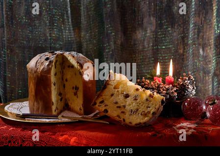 Weihnachts-Panettone mit Scheiben auf einem goldenen Teller, mit beleuchteten Kerzen und Dekorationen in der Nähe. Typisch italienisches Dessert Stockfoto