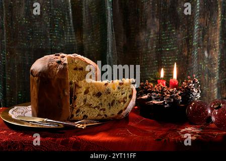 Weihnachts-Panettone mit Scheiben auf einem goldenen Teller, mit beleuchteten Kerzen und Dekorationen in der Nähe. Typisch italienisches Dessert Stockfoto