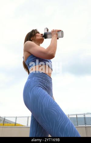 Die Frau in blauer Sportkleidung stillt ihren Durst mit einer Wasserflasche und betont die Notwendigkeit einer richtigen Flüssigkeitszufuhr bei Fitnessübungen. Erfrischung Stockfoto