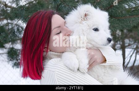 Eine Frau hält einen flauschigen weißen Hund in ihren Armen. Die Frau trägt einen weißen Pullover. Die Szene ist gemütlich und warm, mit der Frau und dem Hund Sharin Stockfoto